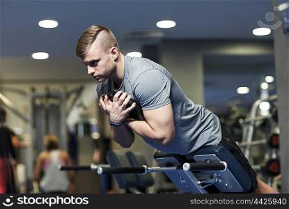 sport, fitness, bodybuilding, lifestyle and people concept - young man flexing back and abdominal muscles on bench in gym