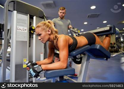 sport, fitness, bodybuilding, teamwork and people concept - young woman and personal trainer flexing muscles on leg curl machine in gym