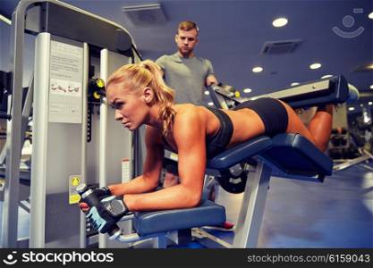 sport, fitness, bodybuilding, teamwork and people concept - young woman and personal trainer flexing muscles on leg curl machine in gym