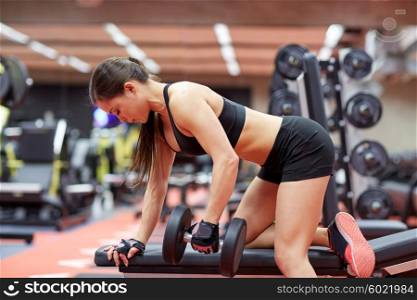 sport, fitness, bodybuilding, weightlifting and people concept - young woman with dumbbell flexing muscles in gym from back