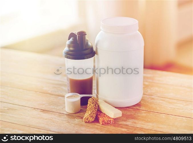 sport, fitness, diet and food concept - close up of jar, protein shake bottle and muesli bars on wooden table
