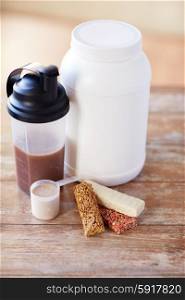 sport, fitness, diet and food concept - close up of jar, protein shake bottle and muesli bars on wooden table