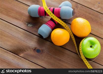 sport, fitness, diet and objects concept - close up of dumbbell and green apple with oranges wrapped by measuring tape on wooden table