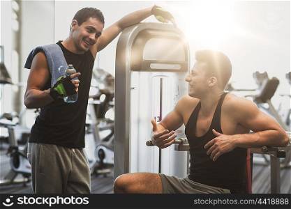 sport, fitness, equipment, lifestyle and people concept - smiling men with bottle of water exercising on gym machine