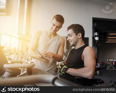 sport, fitness, equipment, technology and people concept - men with tablet pc computer exercising on gym machine