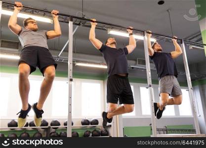 sport, fitness, exercising and people concept - group of young men doing pull-ups on horizontal bar in gym. group of young men doing pull-ups in gym