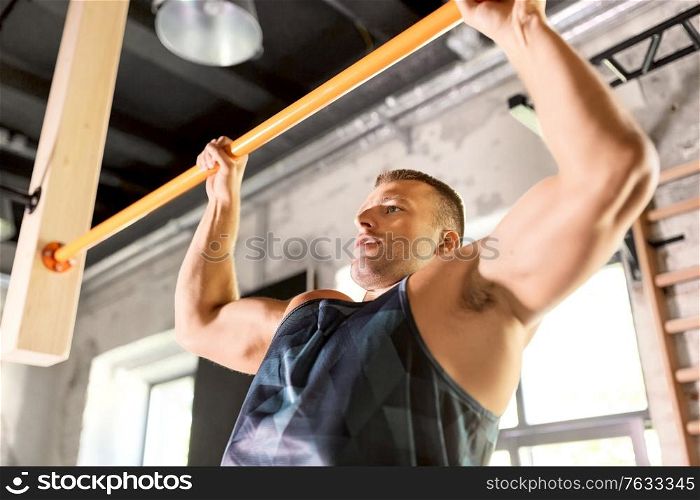 sport, fitness, exercising and people concept - man doing pull-ups on horizontal bar in gym. man exercising on bar and doing pull-ups in gym