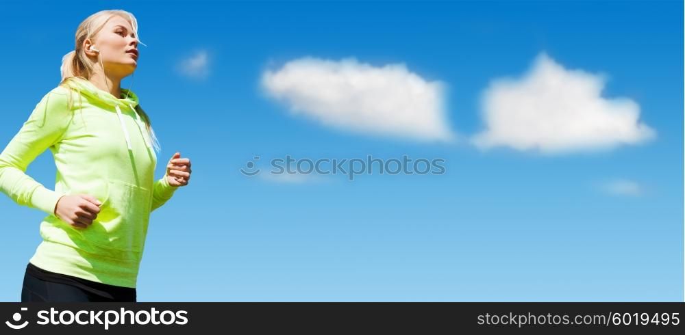 sport, fitness, exercising, people and lifestyle concept - sporty woman with earphones listening to music and running outdoors over blue sky and clouds background
