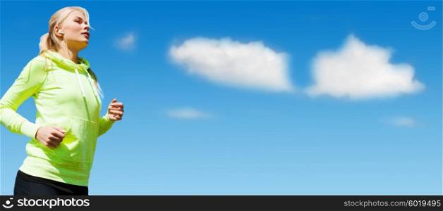 sport, fitness, exercising, people and lifestyle concept - sporty woman with earphones listening to music and running outdoors over blue sky and clouds background