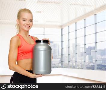 sport, fitness, food additive and people concept - smiling young woman holding protein jar over gym or home background