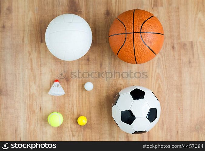 sport, fitness, game, sports equipment and objects concept - close up of different sports balls set and shuttlecock on wooden floor from top