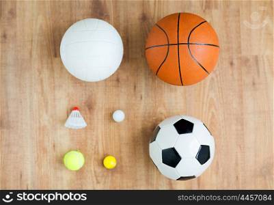 sport, fitness, game, sports equipment and objects concept - close up of different sports balls set and shuttlecock on wooden floor from top