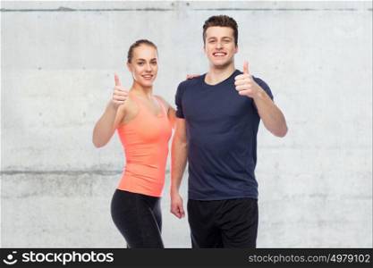 sport, fitness, gesture and people concept - happy sportive man and woman showing thumbs upover concrete wall background. happy sportive man and woman showing thumbs up