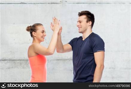 sport, fitness, gesture and people concept - smiling man and woman making high give over concrete wall background. happy sportive man and woman making high five