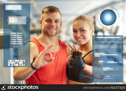 sport, fitness, gesture and people concept - smiling man and woman showing ok hand sign in gym over virtual charts. smiling man and woman showing ok hand sign in gym