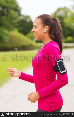 sport, fitness, health, technology and people concept - smiling young african american woman running with smartphone and earphones outdoors