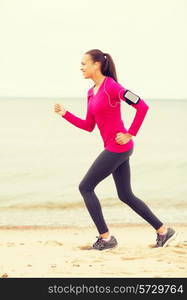 sport, fitness, health, technology and people concept - smiling young african american woman running with smartphone and earphones outdoors