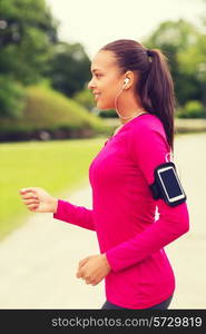 sport, fitness, health, technology and people concept - smiling young african american woman running with smartphone and earphones outdoors