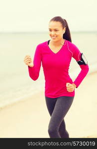 sport, fitness, health, technology and people concept - smiling young african american woman running with smartphone and earphones outdoors