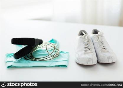 sport, fitness, healthy lifestyle, cardio training and objects concept - close up of sports top, sneakers and skipping rope on table