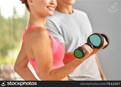 sport, fitness, lifestyle and people concept - close up of smiling woman and personal trainer with dumbbell exercising in gym. close up of smiling woman with dumbbell in gym