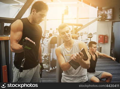 sport, fitness, lifestyle and people concept - men with clipboard taking notes and exercising on gym machine