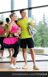 sport, fitness, lifestyle and people concept - smiling couple with water bottles and bags in gym. sportive couple with water bottles and bags in gym