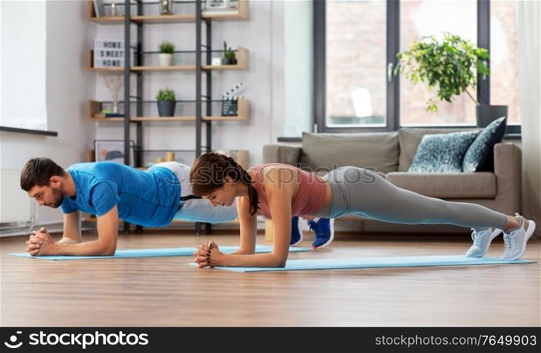sport, fitness, lifestyle and people concept - smiling man and woman exercising and doing plank at home. happy couple exercising at home