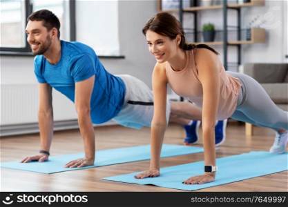 sport, fitness, lifestyle and people concept - smiling man and woman exercising and doing plank at home. happy couple exercising and doing plank at home