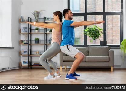 sport, fitness, lifestyle and people concept - smiling man and woman exercising and doing squats at home. happy couple exercising and doing squats at home