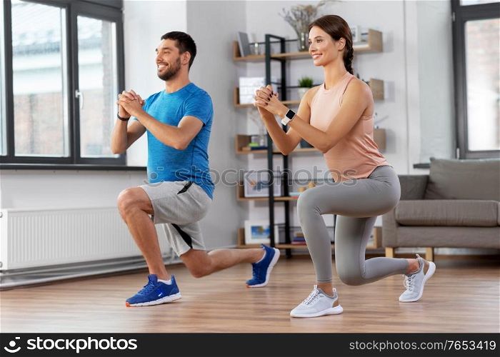 sport, fitness, lifestyle and people concept - smiling man and woman exercising and doing squats in low lunge at home. happy couple exercising and doing squats at home