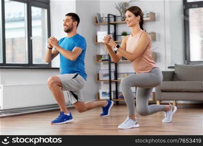 sport, fitness, lifestyle and people concept - smiling man and woman exercising and doing squats in low lunge at home. happy couple exercising and doing squats at home