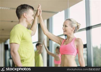 sport, fitness, lifestyle and people concept - smiling man and woman making high five in gym