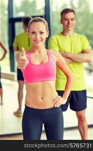sport, fitness, lifestyle and people concept - smiling man and woman showing thumbs up in gym