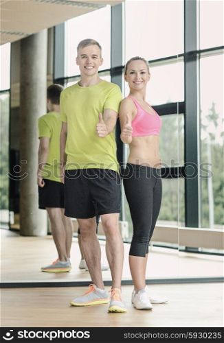 sport, fitness, lifestyle and people concept - smiling man and woman showing thumbs up in gym