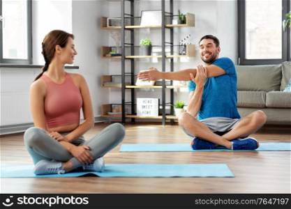 sport, fitness, lifestyle and people concept - smiling man and woman stretching at home. happy couple exercising at home