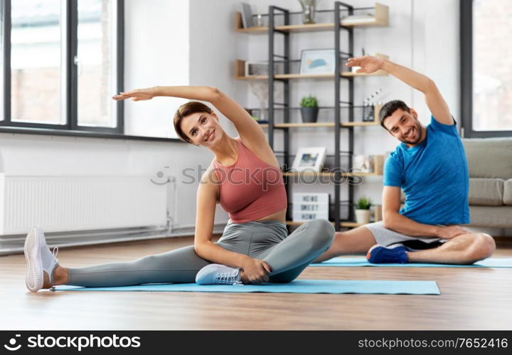 sport, fitness, lifestyle and people concept - smiling man and woman stretching at home. happy couple exercising at home