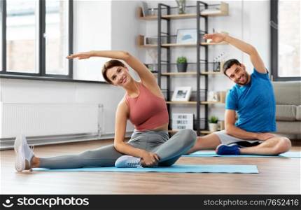 sport, fitness, lifestyle and people concept - smiling man and woman stretching at home. happy couple exercising at home