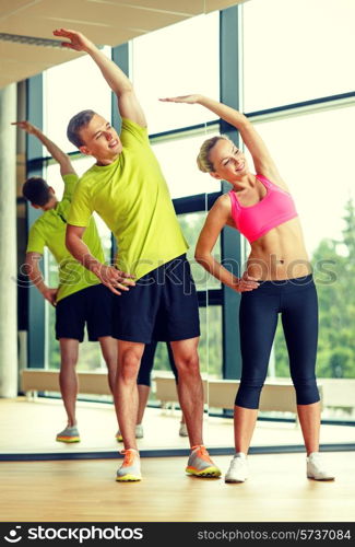 sport, fitness, lifestyle and people concept - smiling man and woman stretching in gym