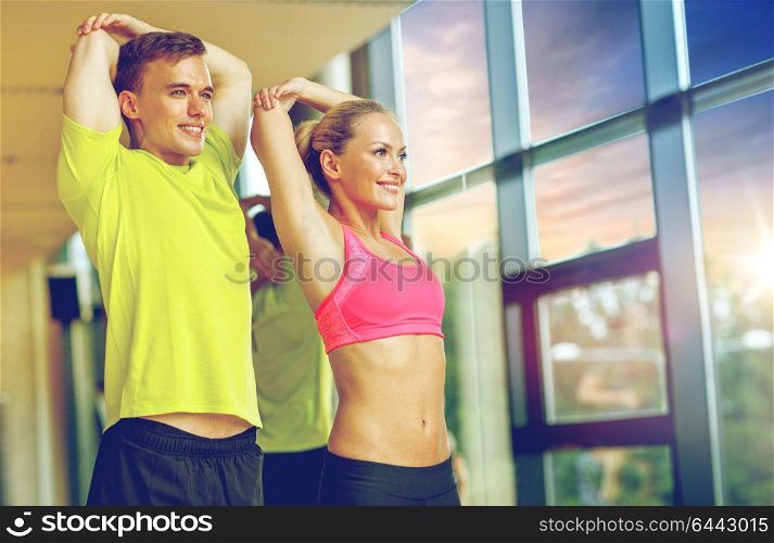 sport, fitness, lifestyle and people concept - smiling man and woman stretching in gym. smiling man and woman exercising in gym