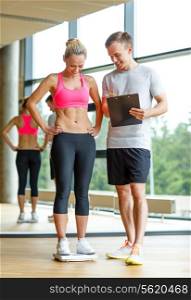 sport, fitness, lifestyle and people concept - smiling man and woman with scales and clipboard in gym