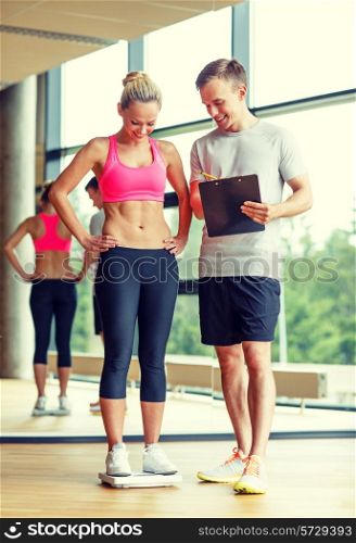 sport, fitness, lifestyle and people concept - smiling man and woman with scales and clipboard in gym