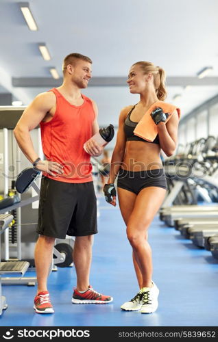 sport, fitness, lifestyle and people concept - smiling man and woman with protein shake bottle and towel talking in gym