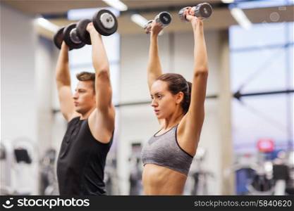 sport, fitness, lifestyle and people concept - smiling man and woman with dumbbells flexing muscles in gym
