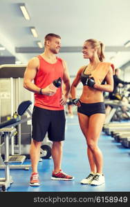 sport, fitness, lifestyle and people concept - smiling man and woman with protein shake bottle and towel talking in gym