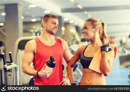 sport, fitness, lifestyle and people concept - smiling man and woman with protein shake bottle and towel talking in gym