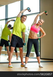 sport, fitness, lifestyle and people concept - smiling man and woman with dumbbells exercising in gym