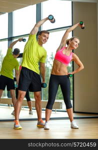 sport, fitness, lifestyle and people concept - smiling man and woman with dumbbells exercising in gym