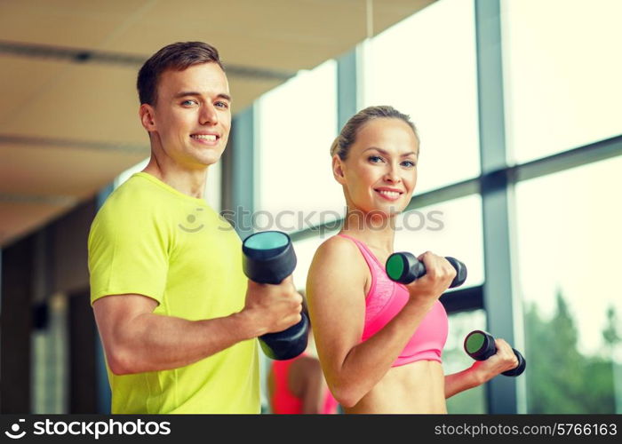 sport, fitness, lifestyle and people concept - smiling man and woman with dumbbells exercising in gym