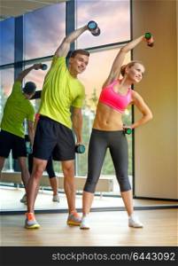 sport, fitness, lifestyle and people concept - smiling man and woman with dumbbells exercising in gym. smiling man and woman with dumbbells in gym